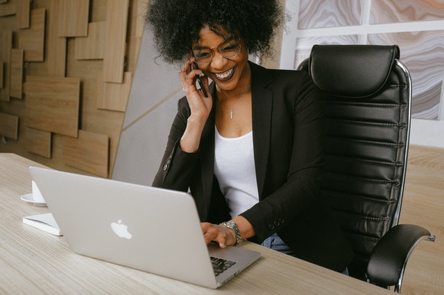 Woman in an office looking at her laptop. She is smiling and talking on her phone.